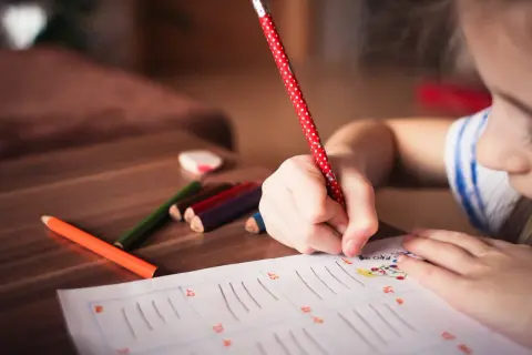 Dziecko pisze kredkami na kartce papieru.