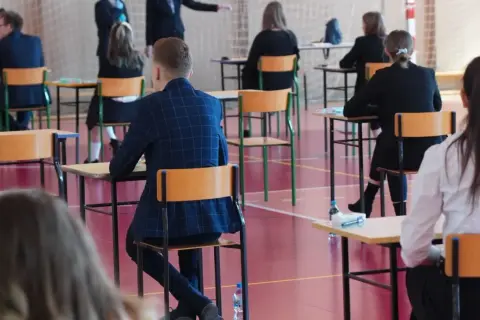 Uczniowie siedzą przy ławkach w sali gimnastycznej podczas egzaminu.