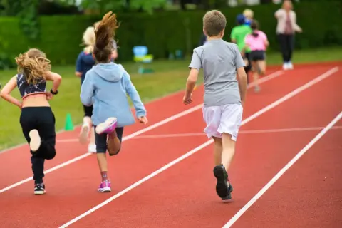 Dzieci biegnące po bieżni lekkoatletycznej podczas lekcji wychowania fizycznego.