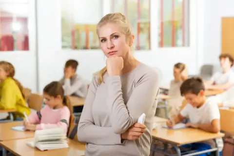 Nauczycielka zamyślona w klasie, gdzie uczniowie piszą. Czy to znak, że godziny ponadwymiarowe nauczycieli są nieuniknione?