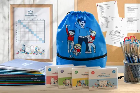 Ramka z tabelą, niebieski worek z postaciami, stos książek i pudełka z grami edukacyjnymi.