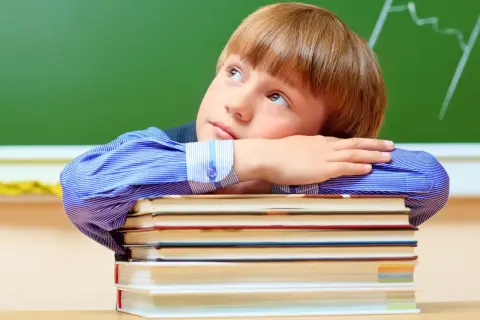 Chłopiec w niebieskiej koszuli opiera głowę na stosie książek, patrząc w górę.