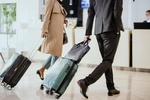 Biznesmeni z walizkami w hotelowym lobby, gotowi na polecenie wyjazdu służbowego.