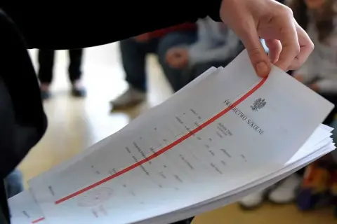 Dłoń trzyma stos świadectw szkolnych z czerwoną linią.