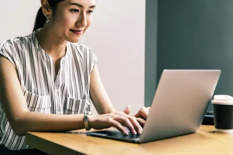 Kobieta z uśmiechem pracuje na laptopie, realizując przygotowanie pedagogiczne online.