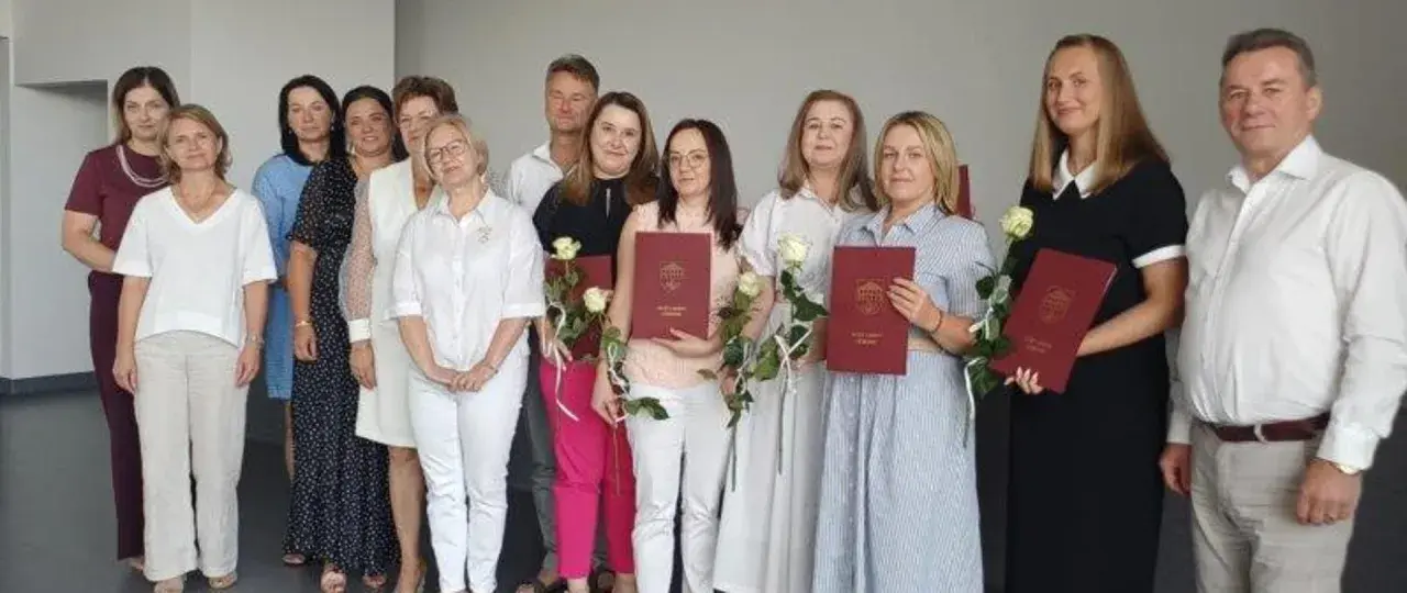 Grupa osób pozuje do zdjęcia, trzymając dyplomy i róże.