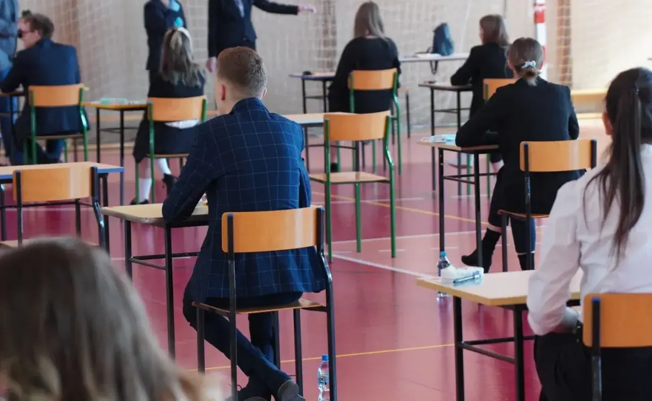 Uczniowie siedzą przy ławkach w sali gimnastycznej podczas egzaminu.