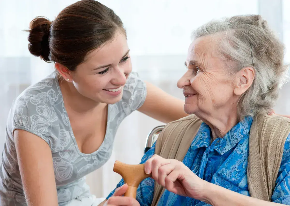Młoda kobieta wspiera starszą panią, która trzyma laskę. To obraz troski i wsparcia, jak podczas 5 dni urlopu opiekuńczego.