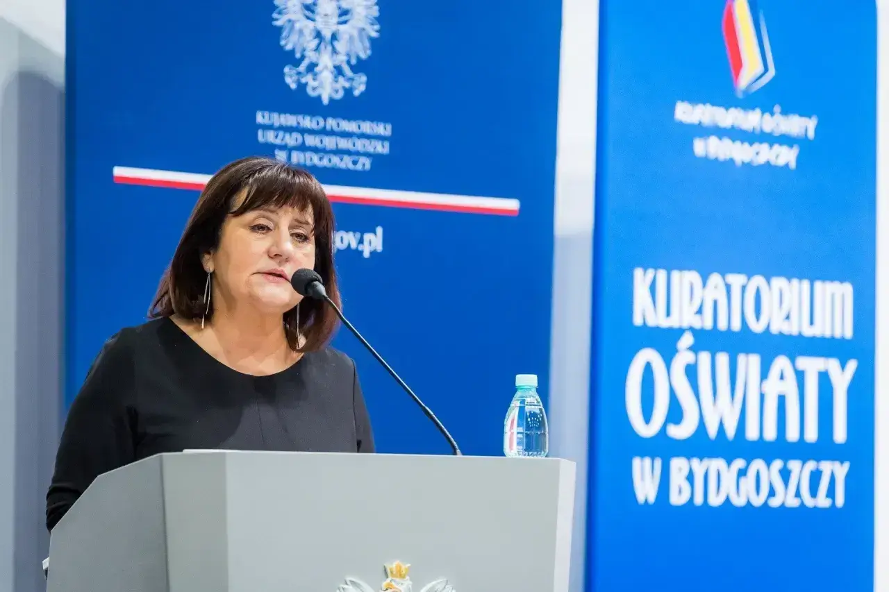Kobieta przemawia przy mównicy. Dowiadujemy się, jak napisać wniosek o nagrodę kuratora oświaty.