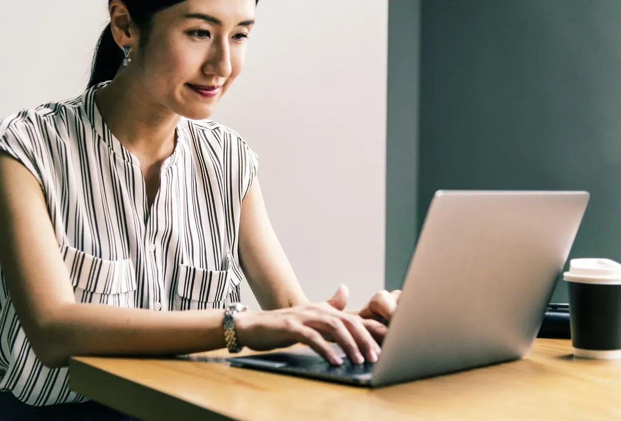 Kobieta z uśmiechem pracuje na laptopie, realizując przygotowanie pedagogiczne online.