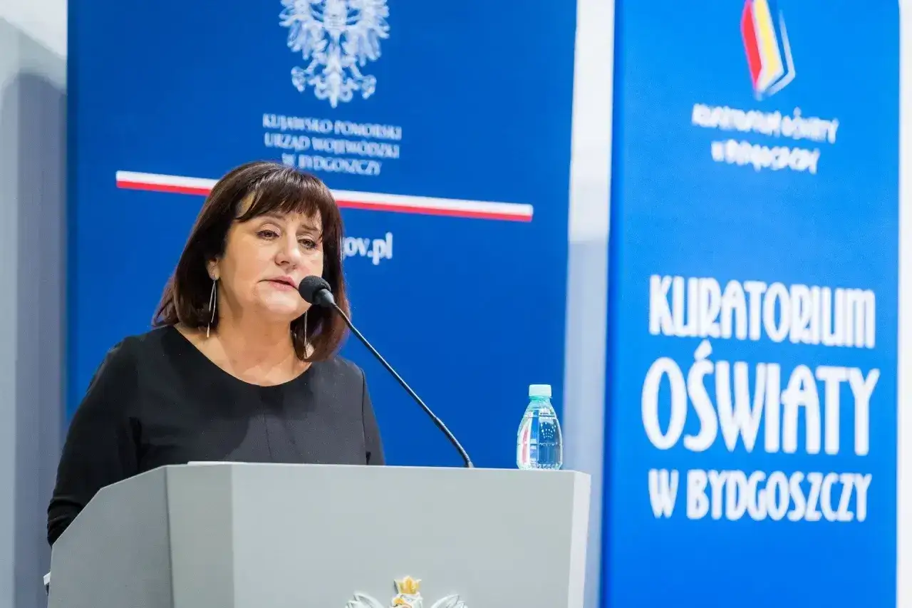 Kobieta przemawia przy mównicy. Dowiadujemy się, jak napisać wniosek o nagrodę kuratora oświaty.
