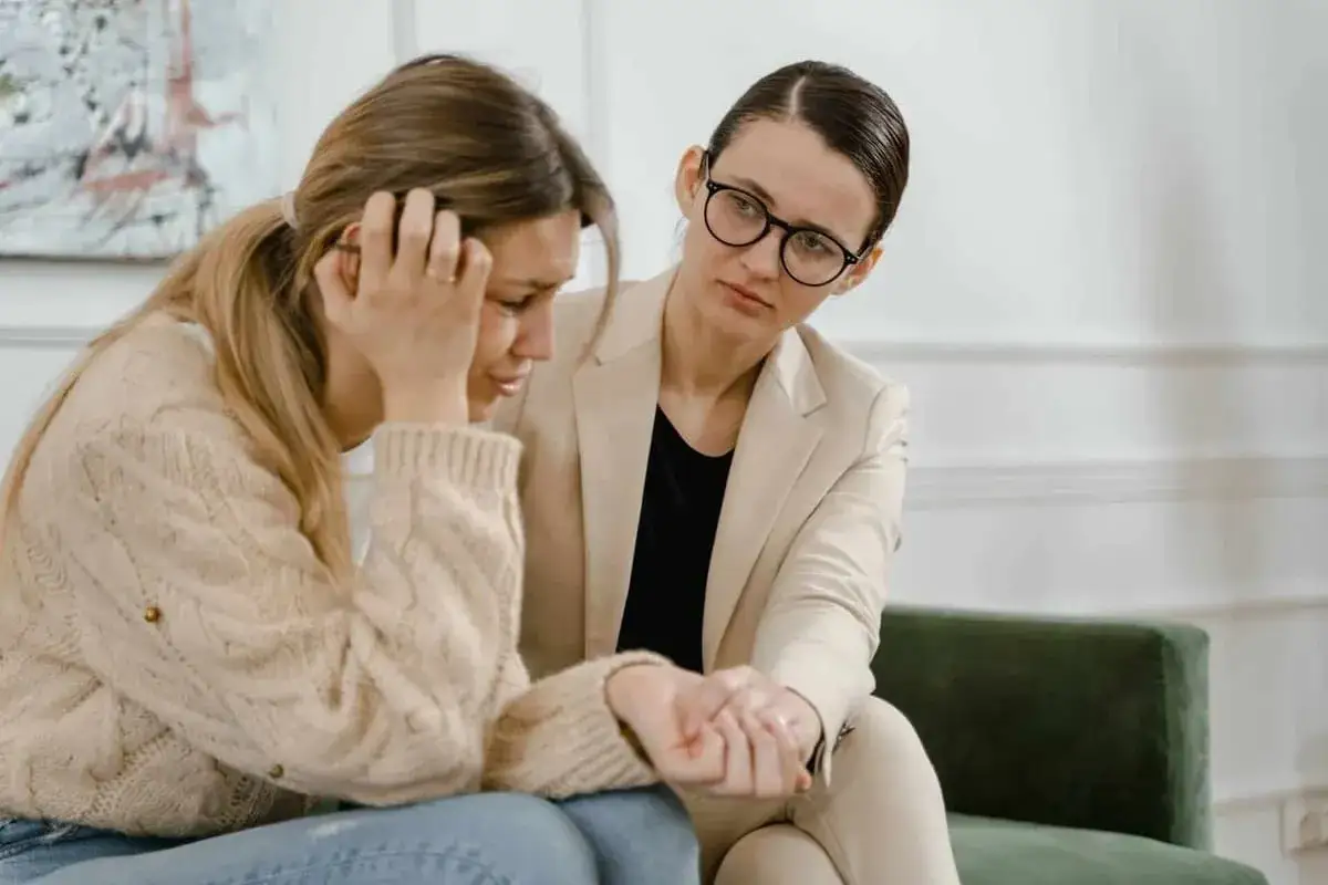 Kobieta w beżowym żakiecie pociesza zapłakaną przyjaciółkę. Czasem nawet urlop siła wyższa nie chroni przed trudnymi emocjami.