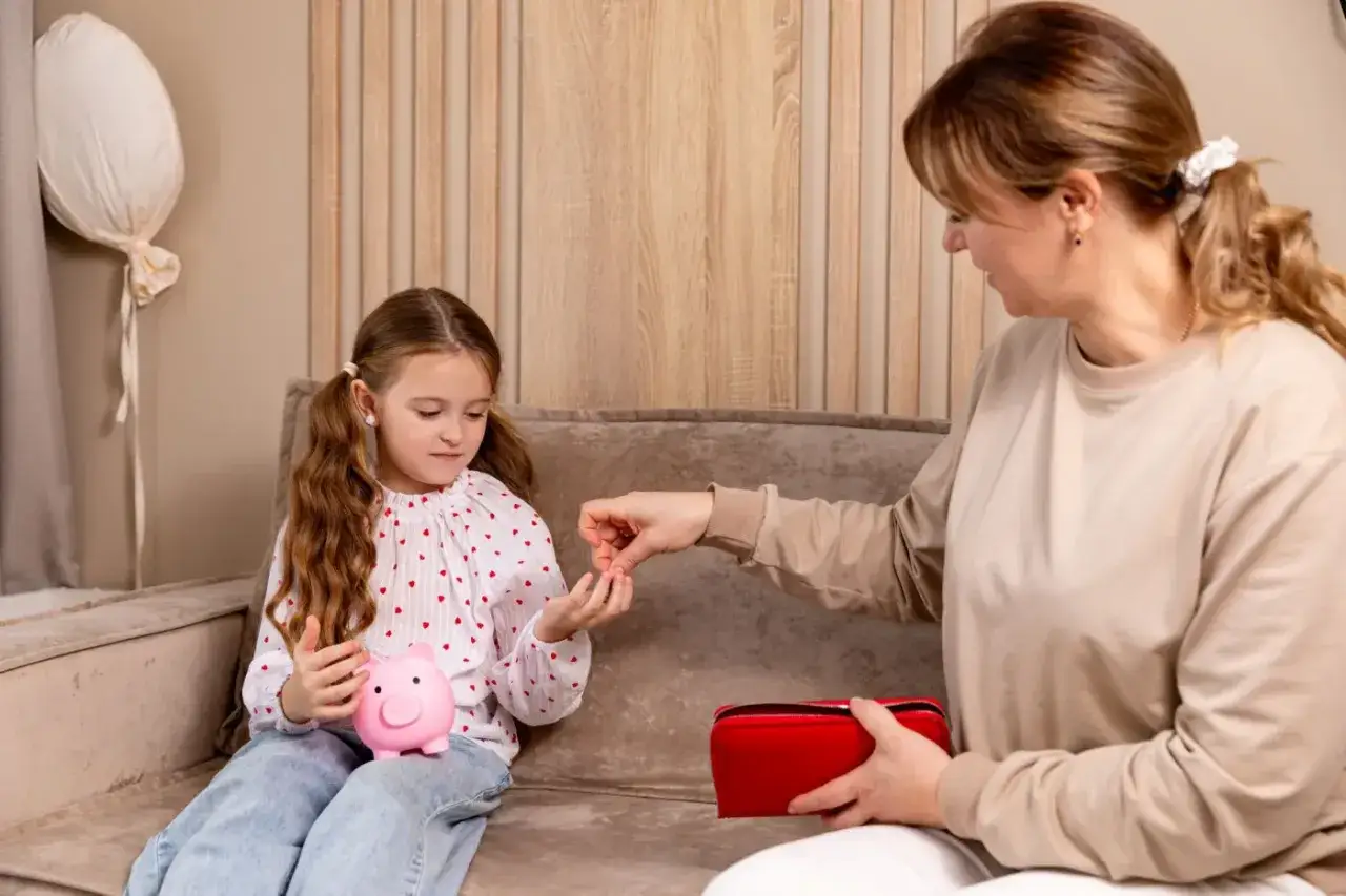 Mama uczy córkę oszczędzać, wrzucając monety do świnki-skarbonki. Czy urlop wychowawczy jest płatny? To pytanie, na które odpowiedź zależy od wielu czynników.