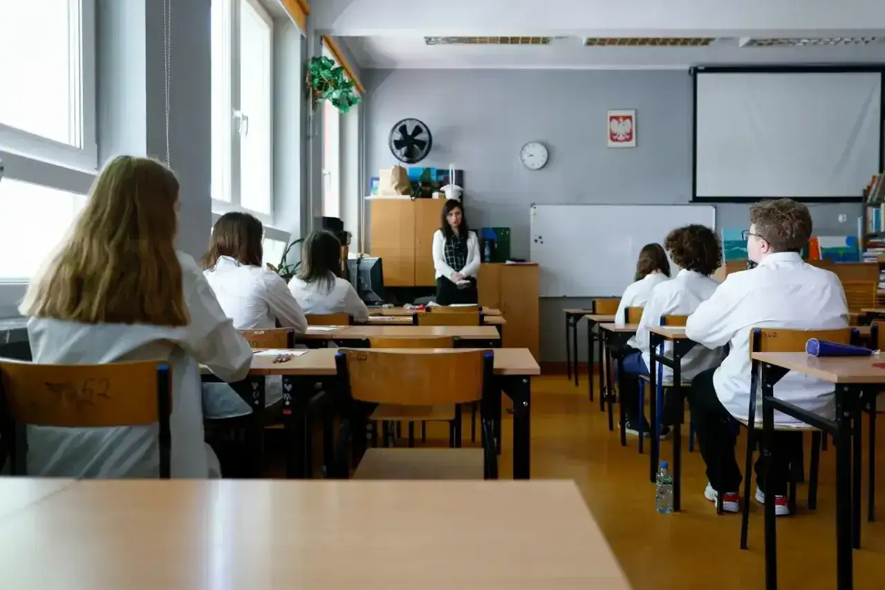 Lekcja w szkole. Nauczycielka stoi przed klasą, uczniowie siedzą w ławkach. Czy uczeń nieklasyfikowany jest promowany?