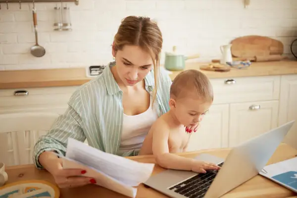 Mama z dzieckiem przy laptopie, analizuje dokumenty. Zastanawia się, urlop rodzicielski ile płatny, by pogodzić pracę i opiekę.