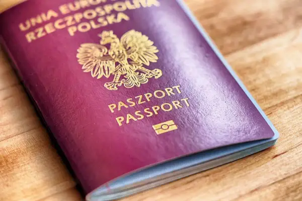 Czerwony paszport z godłem Polski i napisem "PASZPORT" na drewnianym tle.