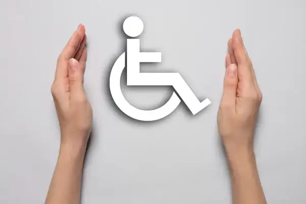 Dwie dłonie otaczają biały symbol osoby na wózku inwalidzkim na jasnoszarym tle.