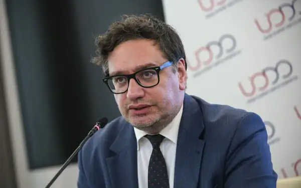Mężczyzna w okularach i garniturze mówi do mikrofonu na tle logo UODO.