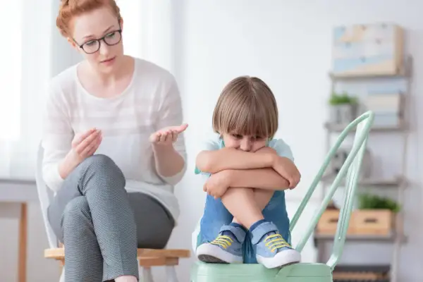 Kobieta w okularach rozmawia ze smutnym chłopcem siedzącym na krześle.