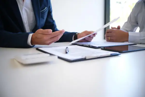 Dwóch mężczyzn omawia dokumenty. Jeden z nich trzyma papier, który może dotyczyć rozwiązania umowy o pracę bez wypowiedzenia.