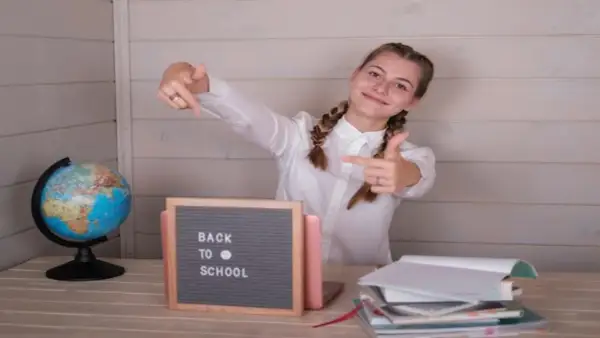 Uśmiechnięta dziewczyna z warkoczami wskazuje palcami na tabliczkę "Back to School" obok globusa i stosu książek.