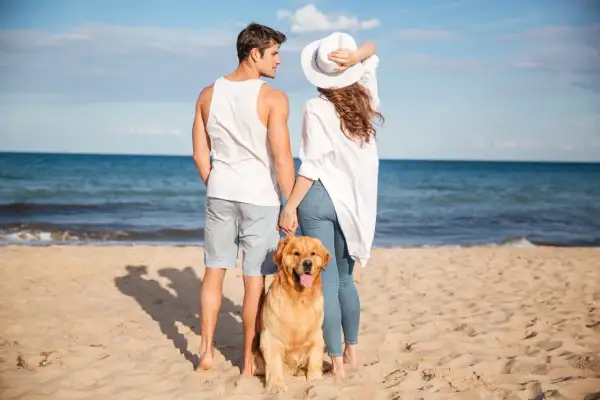 Para młoda z psem na plaży, ciesząca się słońcem. Marzymy, by taki urlop trwał od kiedy 35 dni urlopu.