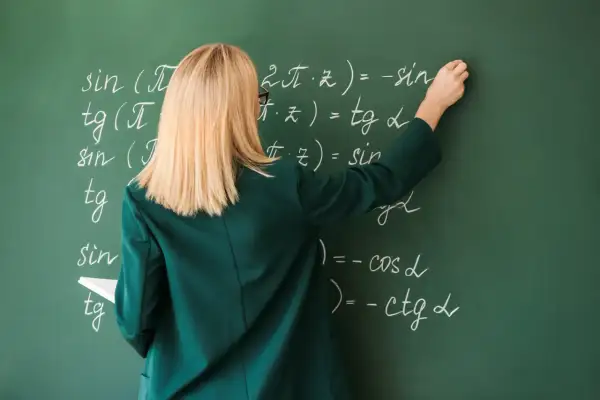 Nauczycielka pisze wzory matematyczne kredą na zielonej tablicy.