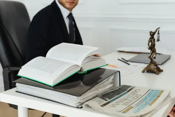 Otwarta księga prawnicza, akta i gazeta na biurku, obok statuetka Temidy.