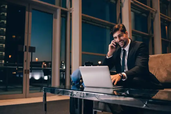 Uśmiechnięty biznesmen rozmawia przez telefon, pracując przy laptopie. Nawet w podróży dba o swoją **dietę krajową**, wybierając zdrowe opcje.