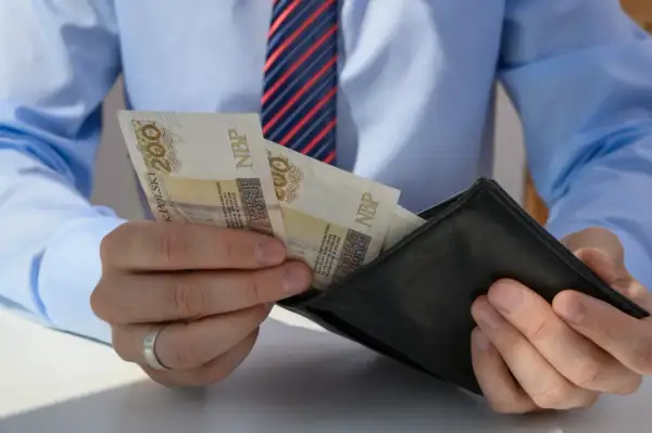Mężczyzna w koszuli i krawacie wkłada polskie banknoty 200 zł do czarnego portfela.