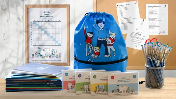 Ramka z tabelą, niebieski worek z postaciami, stos książek i pudełka z grami edukacyjnymi.