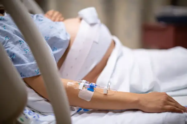 Kobieta w szpitalnym łóżku, z wenflonem w ręce, przechodzi trudny czas urlopu macierzyńskiego po poronieniu.