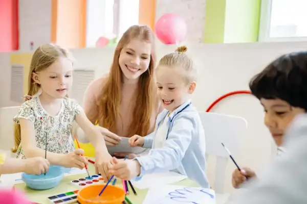 Nauczycielka z dziećmi maluje farbami przy stole w przedszkolu.