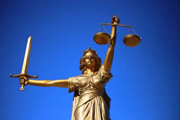 Złota statua Temidy z mieczem i wagą na tle błękitnego nieba.