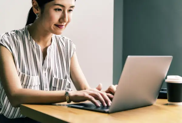 Kobieta z uśmiechem pracuje na laptopie, realizując przygotowanie pedagogiczne online.