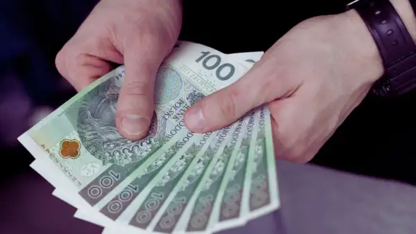 Dłonie trzymają stos banknotów 100 zł. To może być wynagrodzenie młodocianych za ich pierwszą pracę.