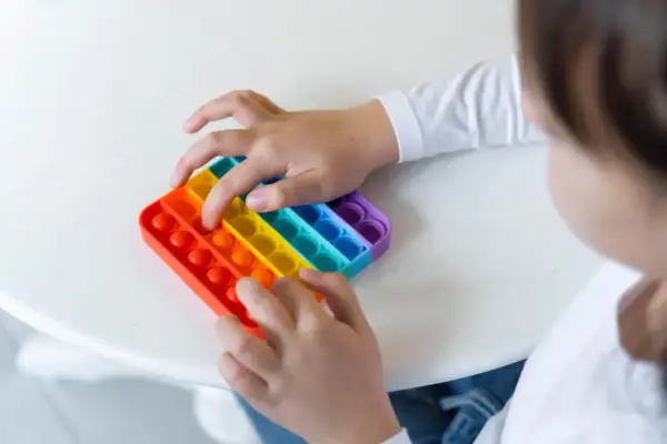 Dziecko bawi się tęczową zabawką sensoryczną typu pop it.